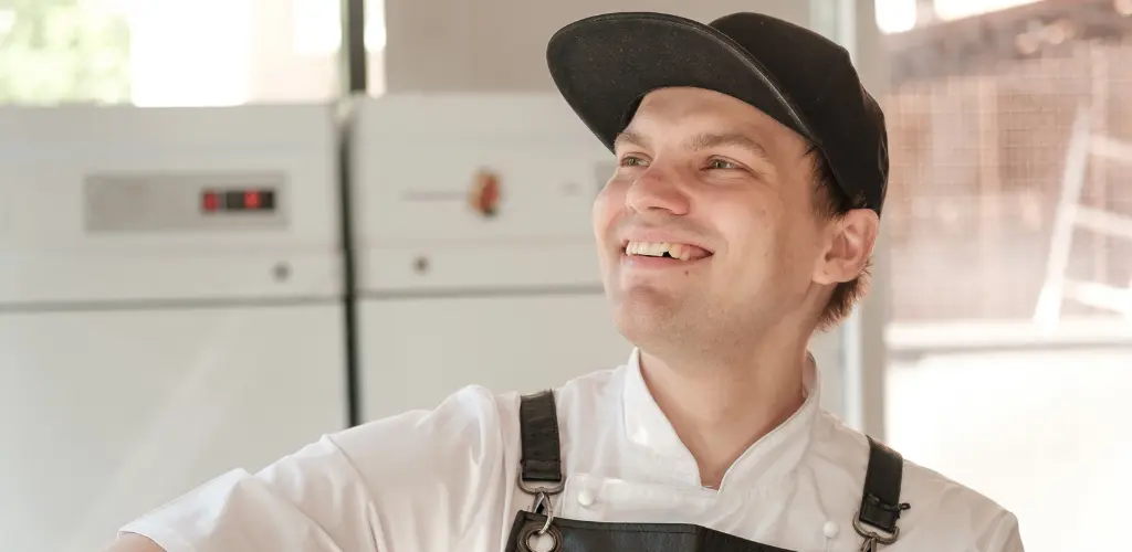 Iloinen yrittäjä lippis päässä keittiössä.